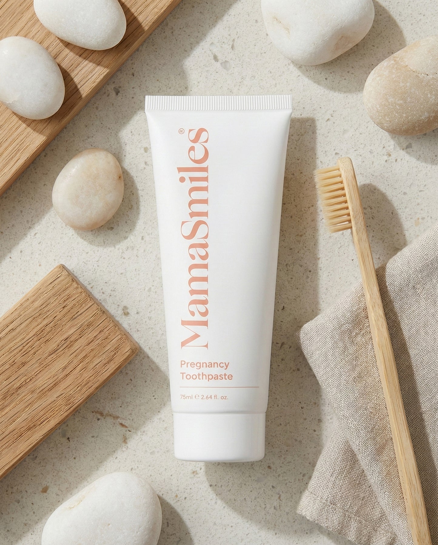 MamaSmiles pregnancy toothpaste tube on a neutral background with a toothbrush and stones.