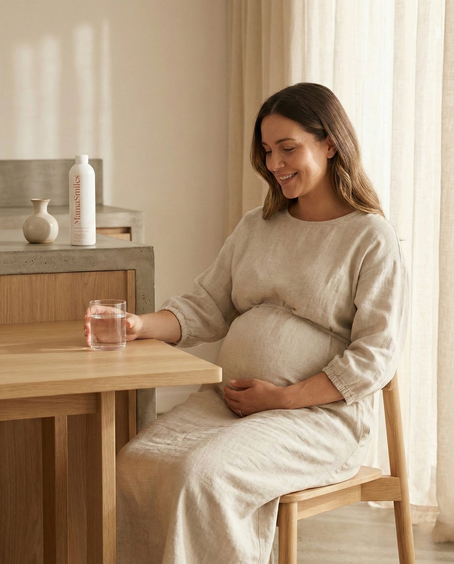 Pregnant woman sitting at a table in a softly lit room, holding her belly and MamaSmiles mouthwash behind