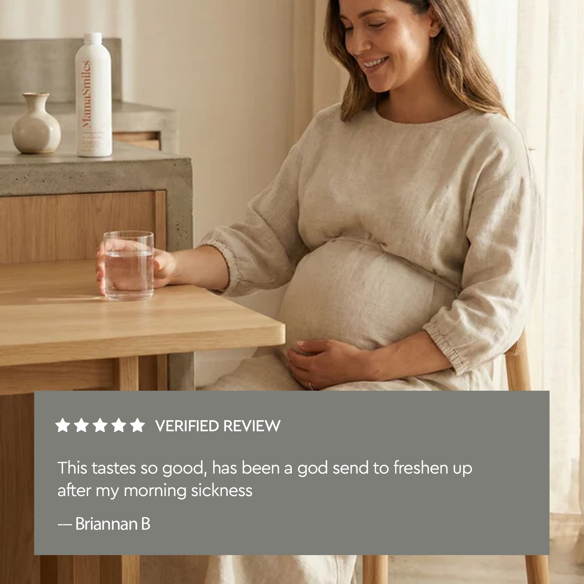 A pregnant woman in a beige linen dress sits at a wooden table, holding a glass of water. A white mouthwash bottle labeled MamaSmiles is visible on a shelf in the background.