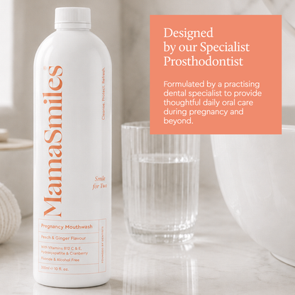 A white bottle of MamaSmiles Pregnancy Mouthwash with orange text, shown next to a glass of water and a white bowl on a light marble surface. An orange text box on the right reads 'Designed by our Specialist Prosthodontist'.