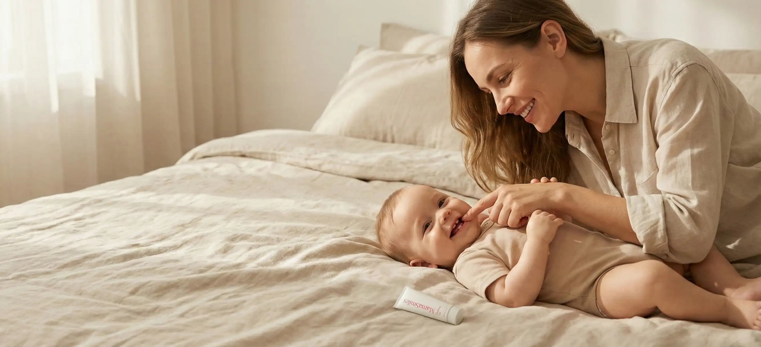 Woman lying on a bed with a baby, both smiling.