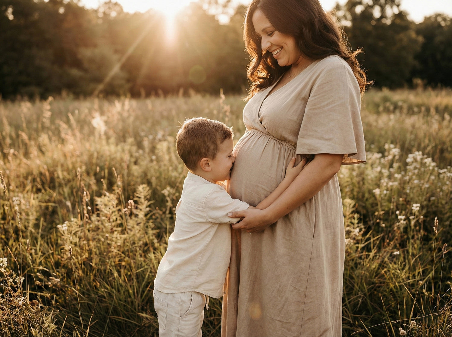 Pregnant woman in a field with a child kissing her belly