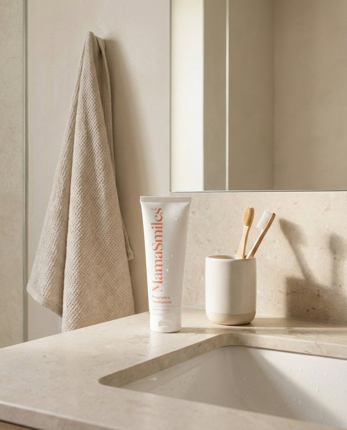 Bathroom counter with a tube of MamaSmiles toothpaste, toothbrushes, and a towel.