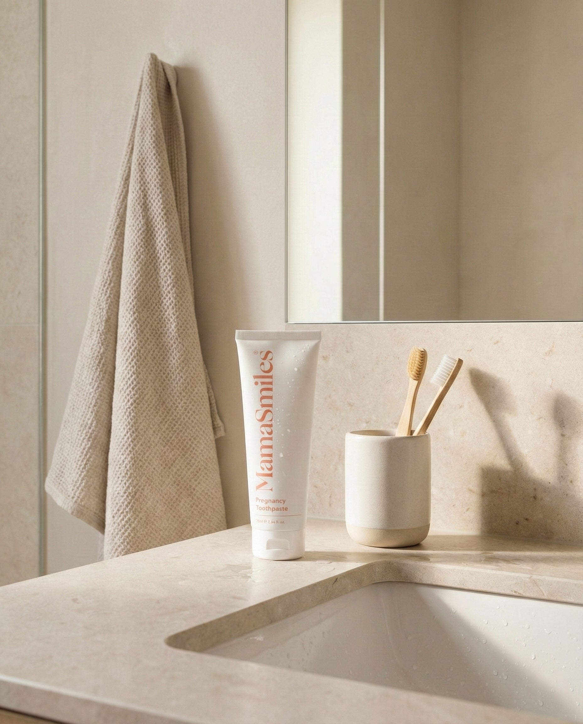 Bathroom counter with a tube of MamaSmiles toothpaste, toothbrushes, and a towel.