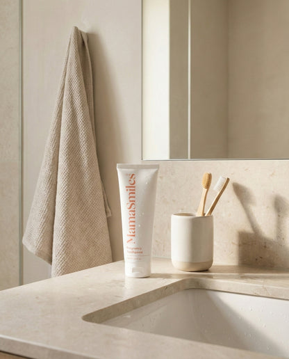 Bathroom counter with a tube of MamaSmiles toothpaste, toothbrushes, and a towel.